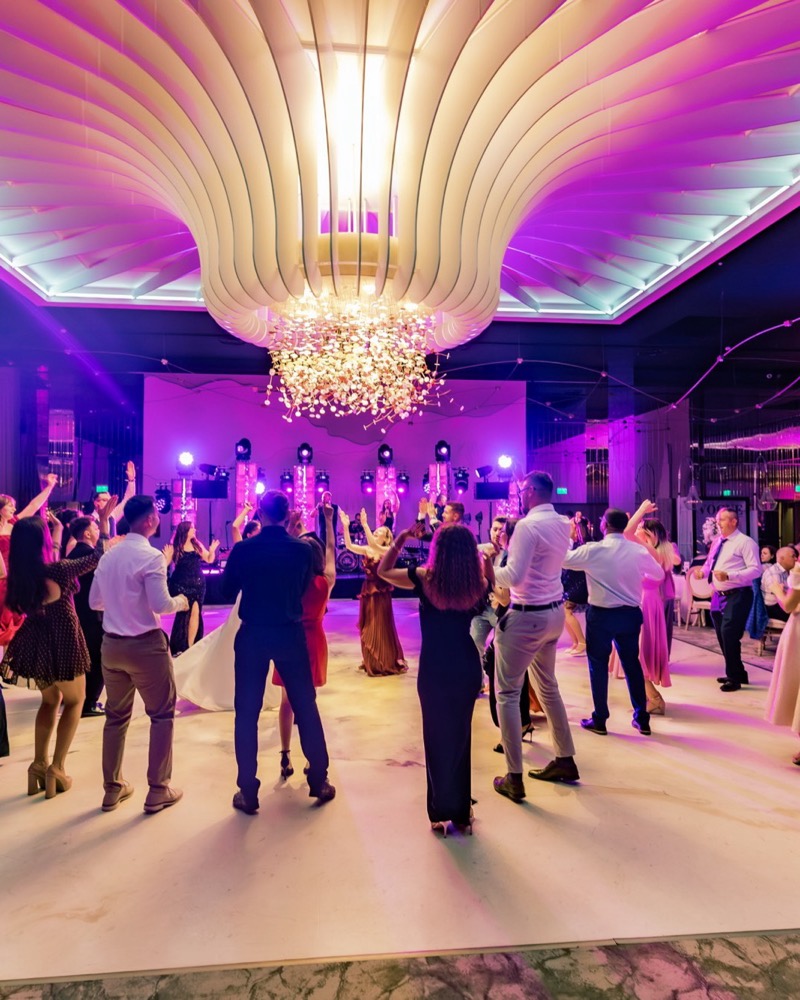Ringul plin sub tavanul sculptat și candelabrul unui salon, cu scena trupei luminată la capătul sălii