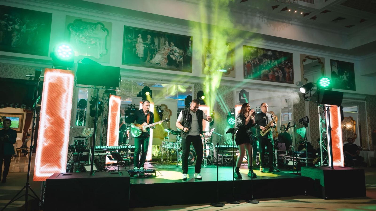 The Fun Station Band cântând la un botez, pe scenă, între stâlpii cu ecrane LED, în lumini verzi