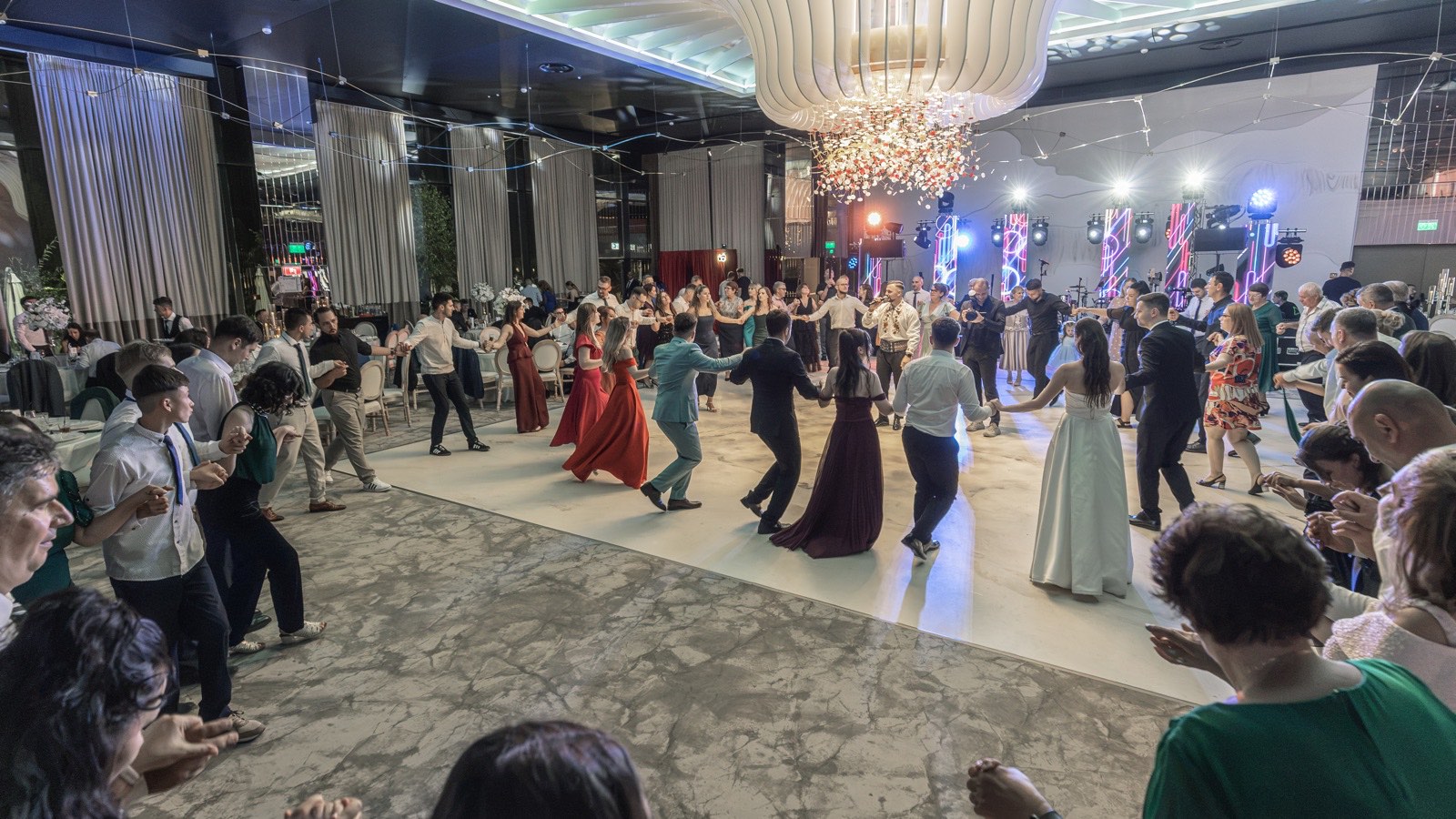 O horă mare pe tot ringul, într-o sală cu candelabru, cu mireasa și Cătălin, solistul de populară, în cerc și ecranele trupei în fundal
