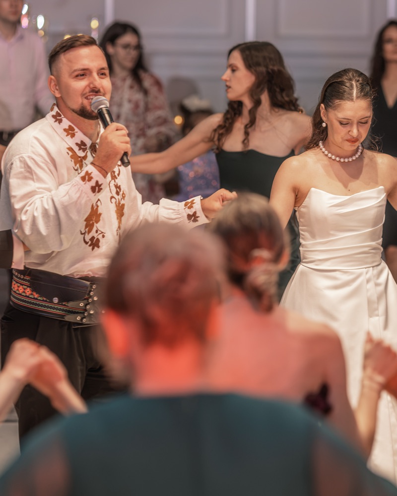 Cătălin, solistul nostru de populară, în ie, cântă cu microfonul în mână lângă mireasă, în mijlocul horei