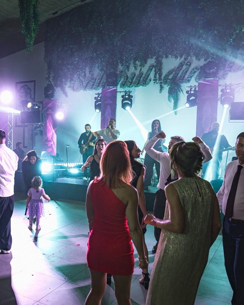 Ringul plin în fața scenei: invitați de toate vârstele dansează, o fetiță printre ei, iar trupa cântă în lumini mov și turcoaz