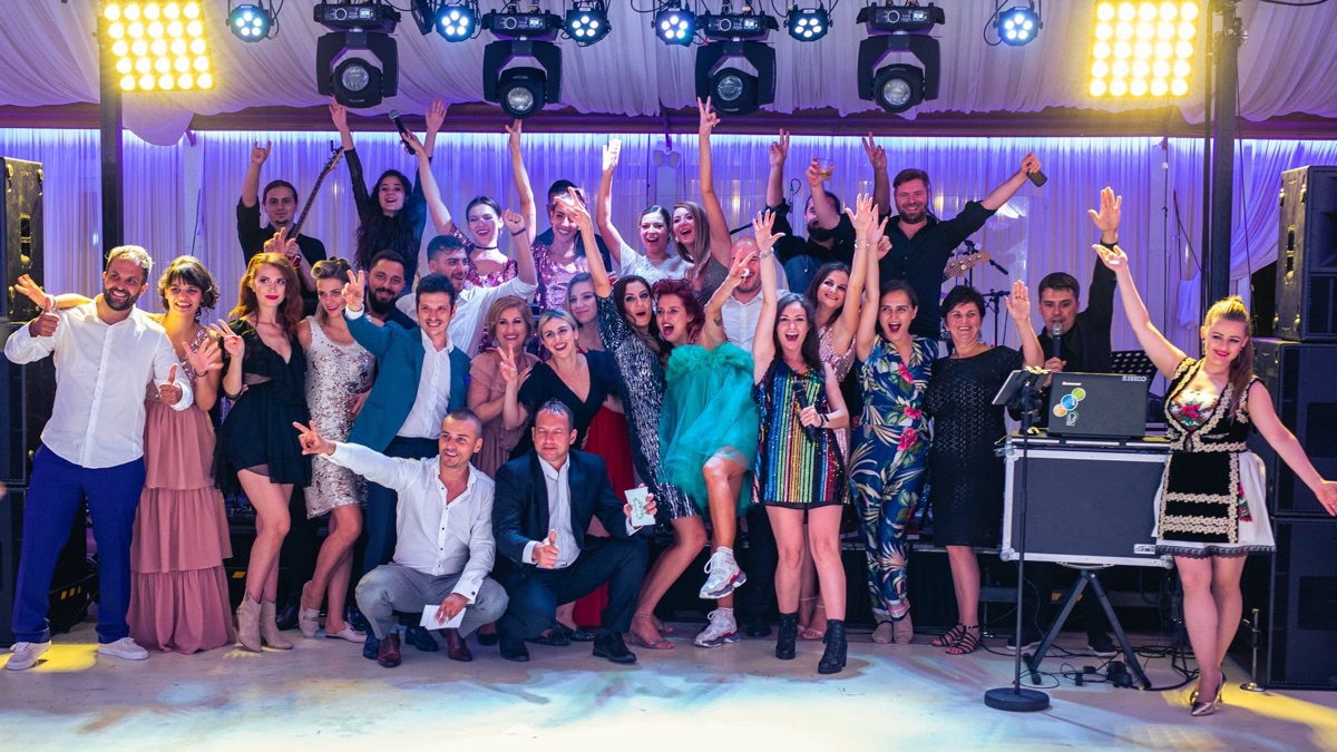 Trupa, DJ-ul și solista de muzică populară, împreună cu invitații, cu mâinile ridicate în fața scenei