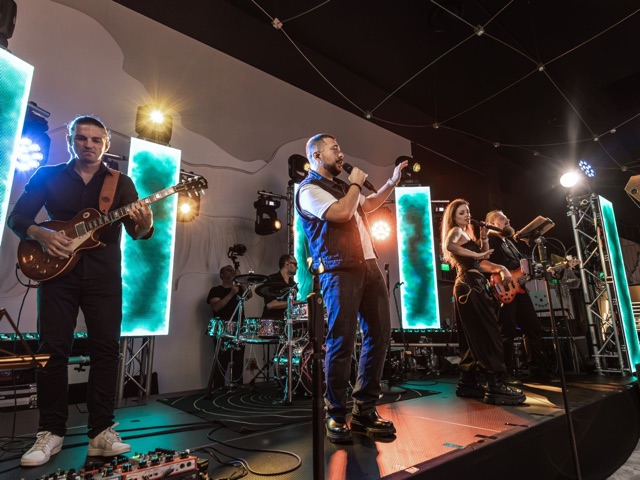 Basistul și solistul pe scenă sub cort, cu ecrane LED și invitați alături