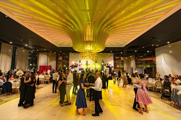 Invitați dansând sub candelabrul salonului, în lumină aurie