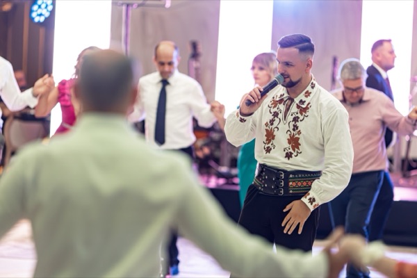 Cătălin cântând în mijlocul invitaților, în cămașă cu motive tradiționale